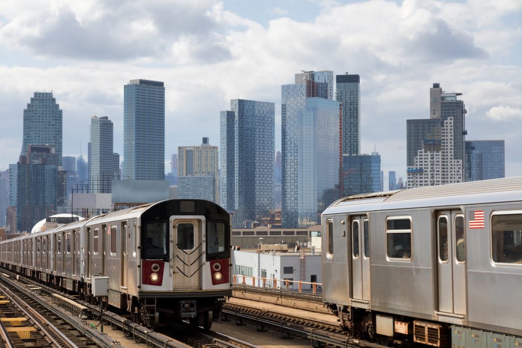 Two subway trains speeding on elevated track in Queens, New York. Financial and residential buildings are seen in background, USA